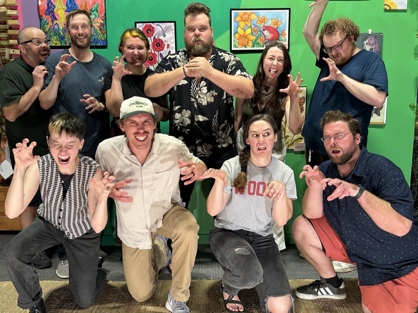 The members of Critter Fight clawing at the camera in front of a green gallery wall